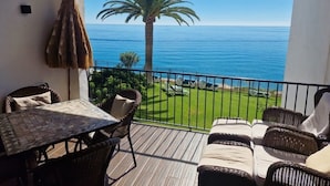 Un balcon doté de meubles en osier, d’une table et offrant une vue sur la mer et les palmiers.