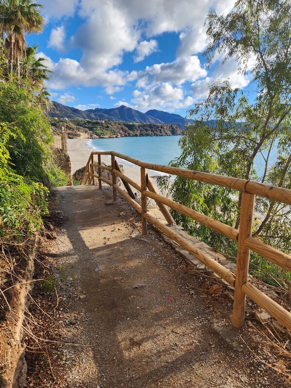 Un sendero de madera que conduce a una playa, con vista despejada al mar y montañas al fondo.