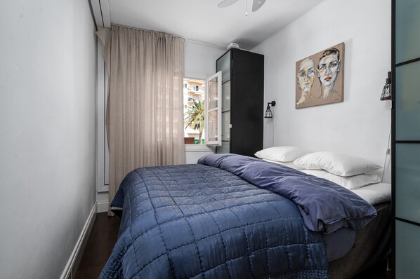 Une chambre à coucher avec un lit, une fenêtre avec des rideaux, un tableau au mur et une petite table de chevet.