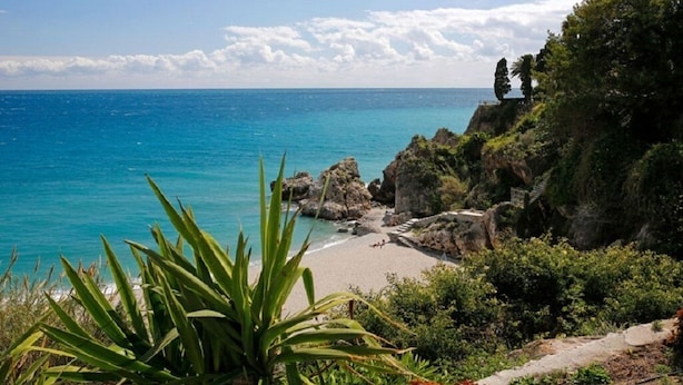 Un paysage côtier comprenant une plage, des affleurements rocheux et une végétation dense.