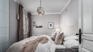 Une chambre à coucher avec un lit, un luminaire suspendu, une table de chevet avec une lampe et un tableau encadré au mur.