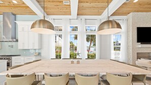A modern kitchen with white cabinets, a large island, and a dining area with a wooden table and chairs. - Bullish on Beaches|Easy Beach Access|Stunning Views|New Construction (Inlet Beach)