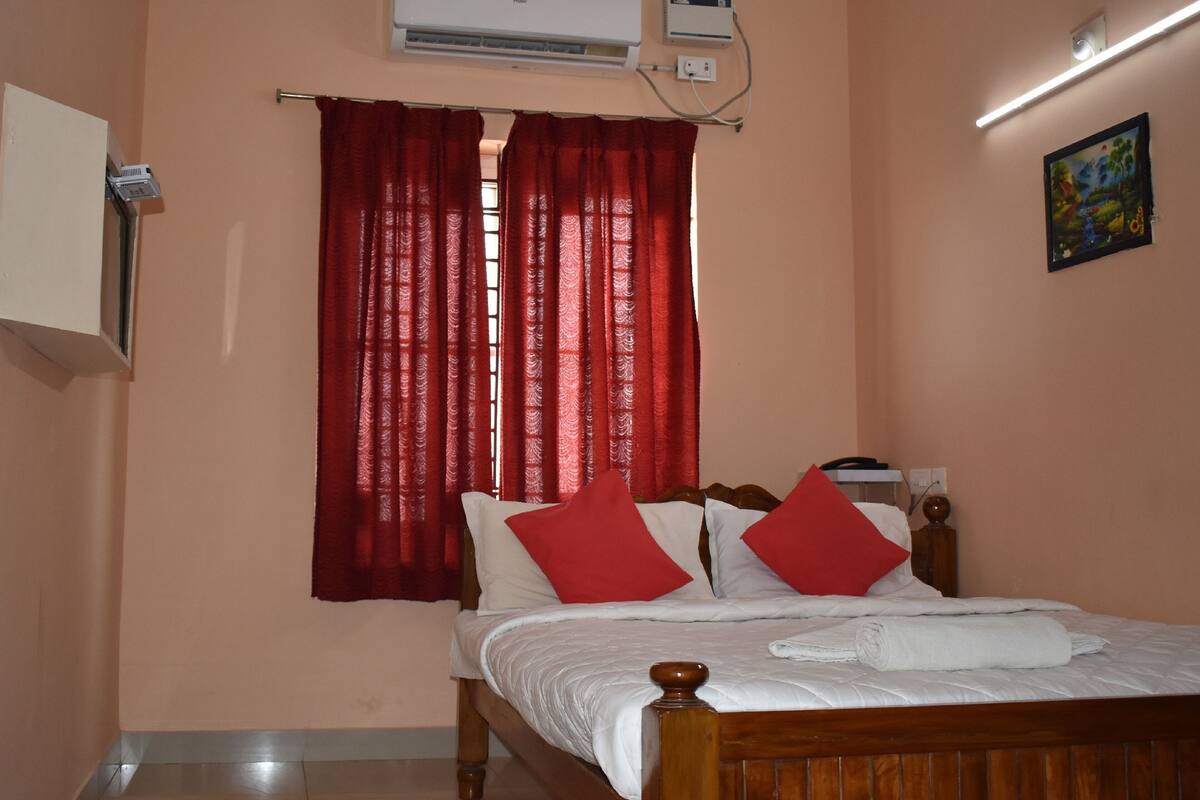 Een slaapkamer met een houten bed, rode gordijnen, een airconditioning en een schilderij aan de muur.