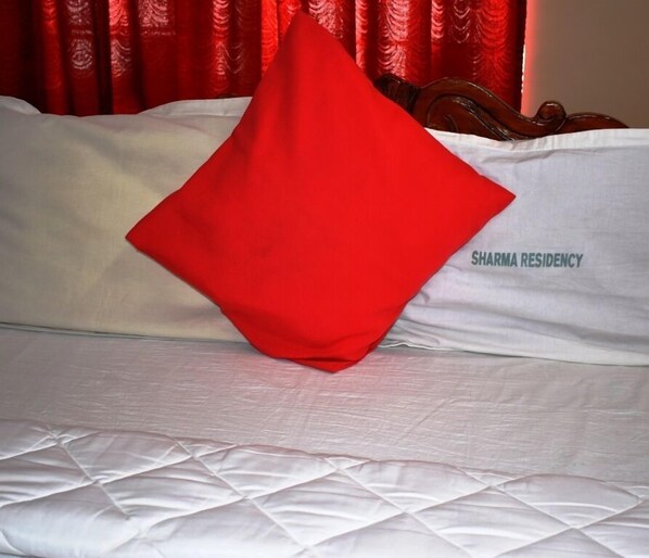 Un lit avec un oreiller rouge et un oreiller blanc portant l’inscription « SHARMA RESIDENCY ».