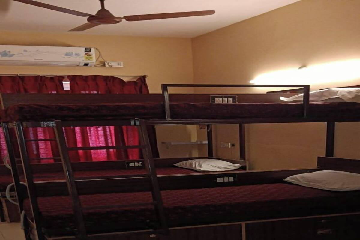 Een slaapkamer met stapelbed, plafondventilator, verwarming en een raam met rode gordijnen.