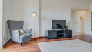 A modern living room with a grey armchair, a black entertainment unit, and a floor lamp. - Bela São Tiago I (Funchal)
