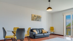 A modern living room with a dining table, two sofas, and a large window. - Bela São Tiago I (Funchal)