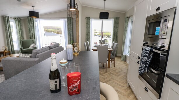 A modern kitchen with a built-in oven, a dining area with a table and chairs, and a seating area with a sofa and armchairs. - 48 Crosswinds (Bembridge)