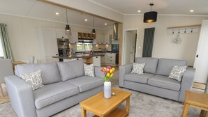 A modern living room with a grey sofa, a wooden coffee table, and a vase of flowers. - 48 Crosswinds (Bembridge)