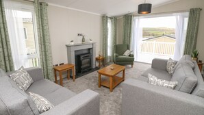 A living room with two grey sofas, a fireplace, and a balcony with a view. - 48 Crosswinds (Bembridge)