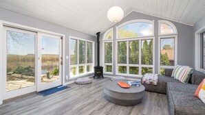 Ett rymligt rum med stora fönster, en öppen spis och en mysig sittgrupp.
