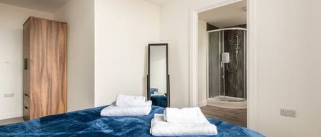 A bedroom with a large bed, a wooden wardrobe, a mirror, and a shower area.