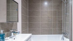 A modern bathroom with a bathtub, a glass shower enclosure, and a vanity with toiletries. - Cozy Manchester 1BR – Perfect for 3 (Salford)