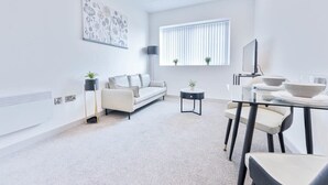 A modern living room with a sofa, a coffee table, a dining table with chairs, a TV, and a window with blinds. - Fantastic 1 Bed Apartment in Wolverhampton (Wolverhampton)