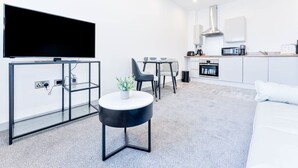 A modern living room with a flat-screen TV, a glass coffee table, and a sofa. There is a kitchen area with a microwave, oven, and cabinets. - Fantastic 1 Bed Apartment in Wolverhampton (Wolverhampton)