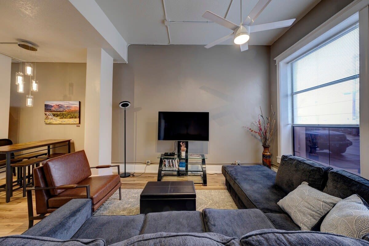 A modern living room with a large flat-screen TV, a sofa, a coffee table, and a dining area with a bench and table.