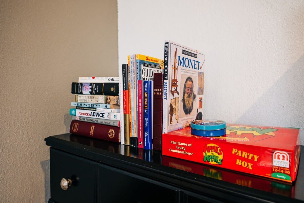 Ein Stapel Bücher auf einem schwarzen Schrank, obenauf eine Gesellschaftsspielbox.