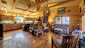 Ein geräumiges Blockhaus-Interieur mit Holzboden, einem großzügigen Essbereich, einem gemütlichen Wohnzimmer mit Kamin und einer Küche mit Holzschränken.