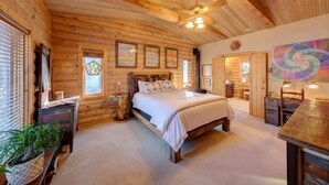 Ein gemütliches Schlafzimmer in einer Blockhütte mit einem Holzbett, einem Deckenventilator und einem großen Fenster mit Aussicht.