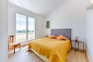 Une chambre avec un grand lit, une fenêtre, une chaise et une petite table.