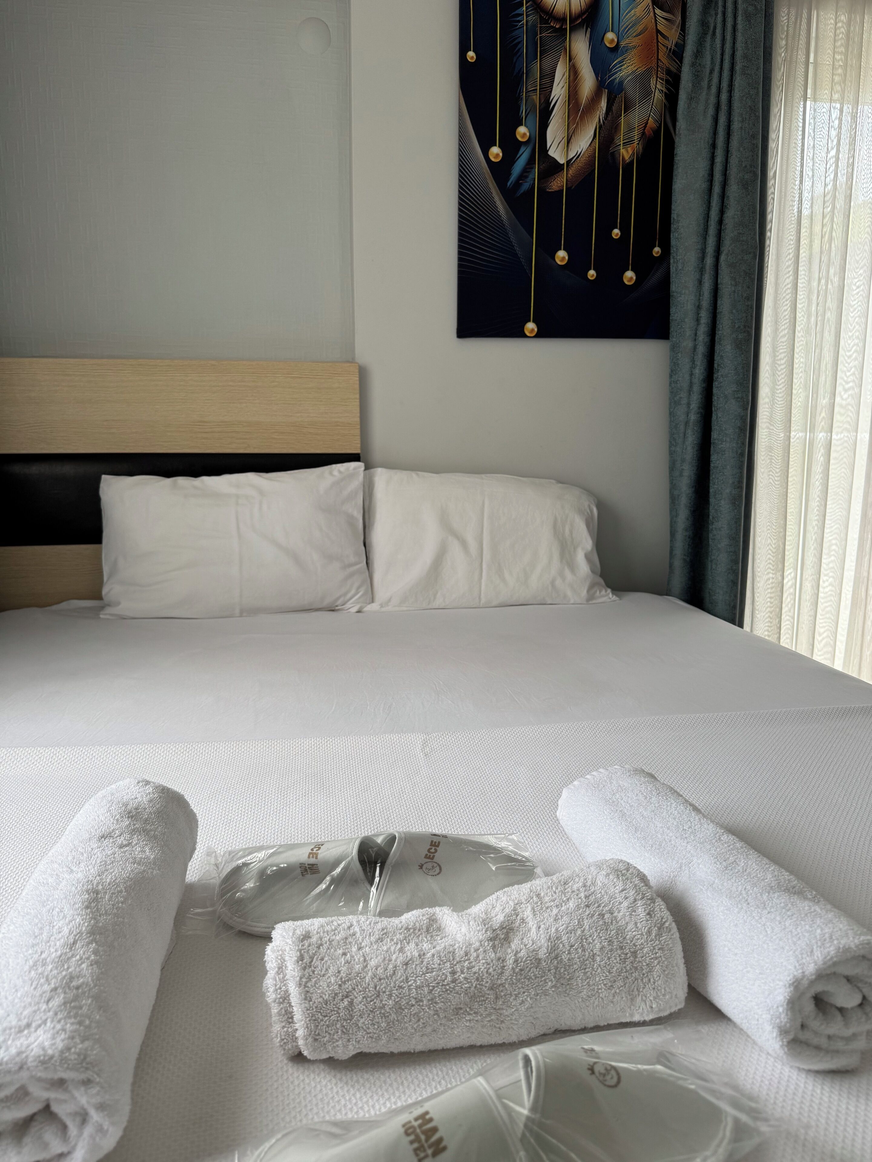 A neatly made bed with white linens, a pillow, and rolled towels.