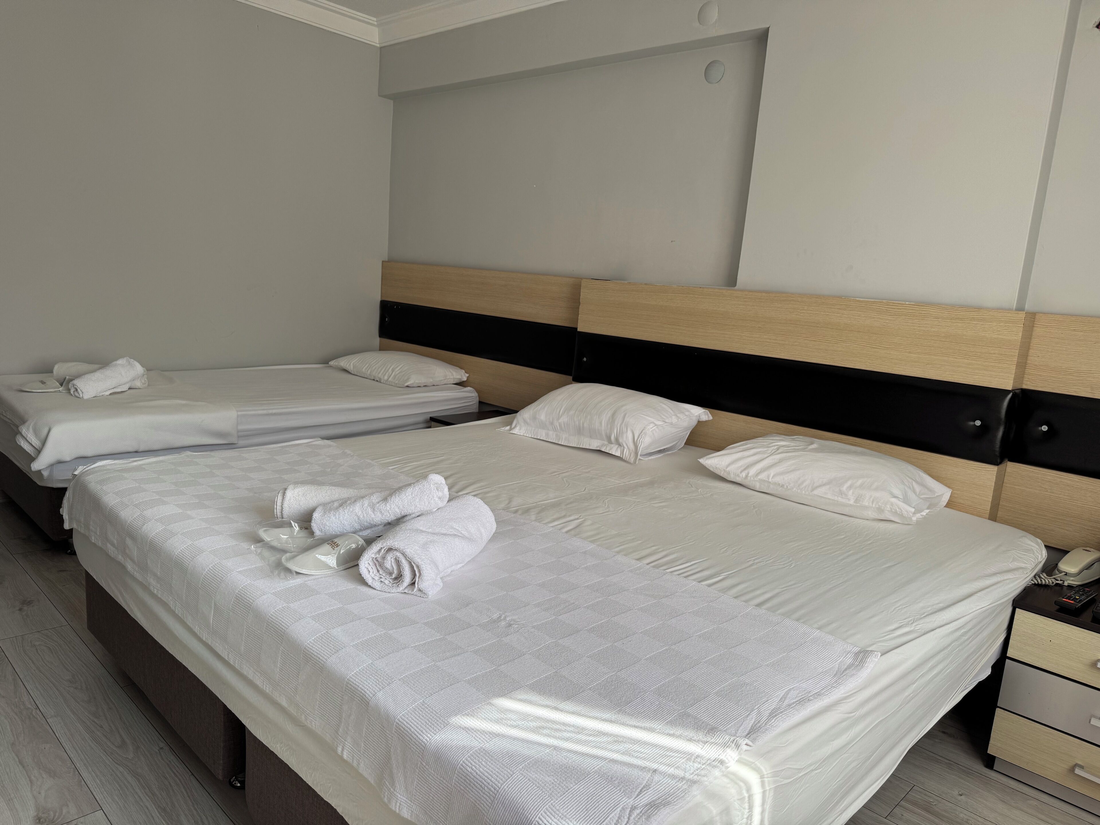 Habitación de hotel con dos camas, cada una con ropa de cama y almohadas blancas, cabeceros de madera y mesitas de noche con teléfono y control remoto.