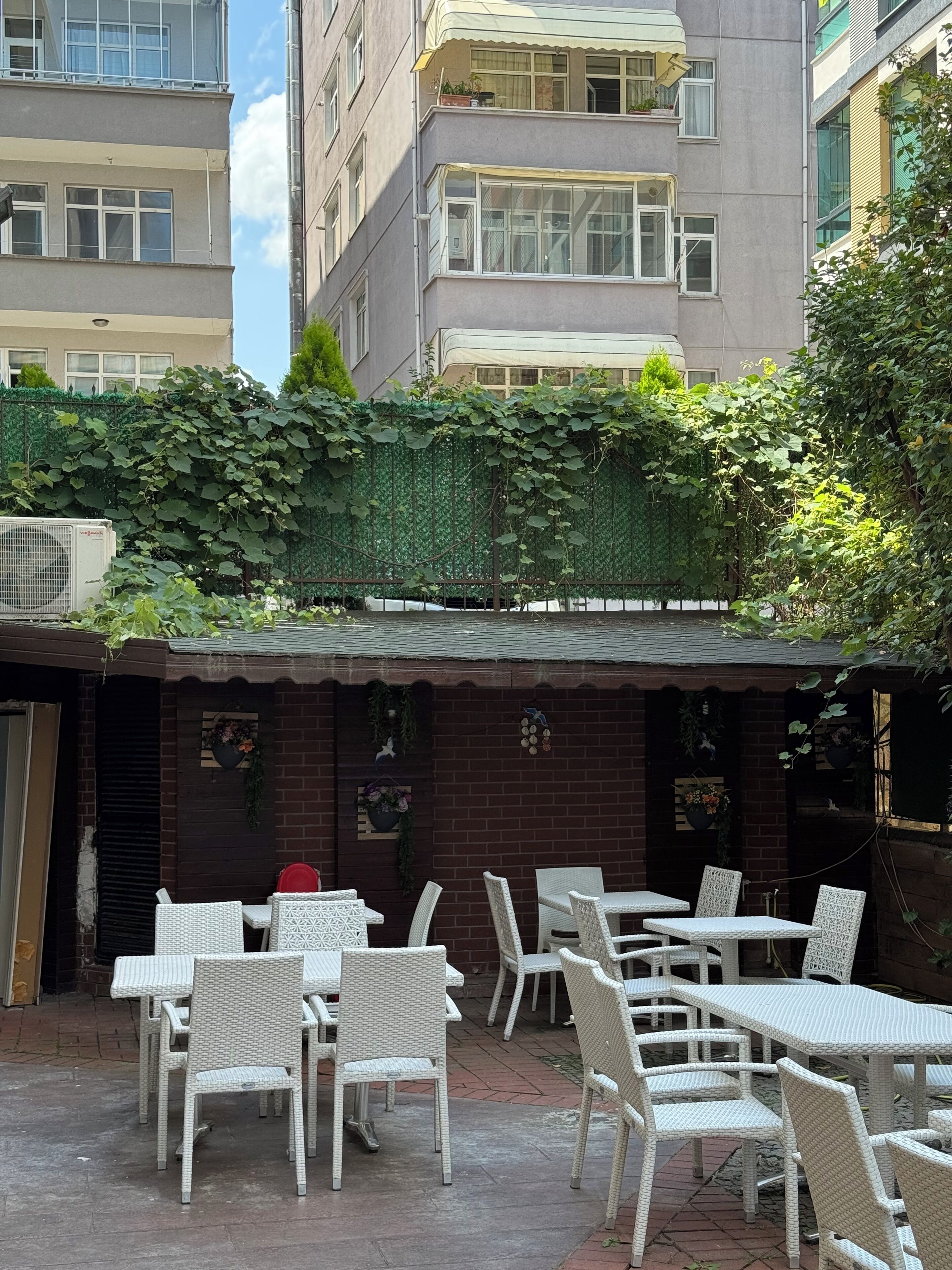 An outdoor patio with white wicker furniture, brick walls, and a green climbing plant.