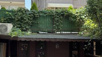 An outdoor patio with white wicker furniture, brick walls, and a green climbing plant.