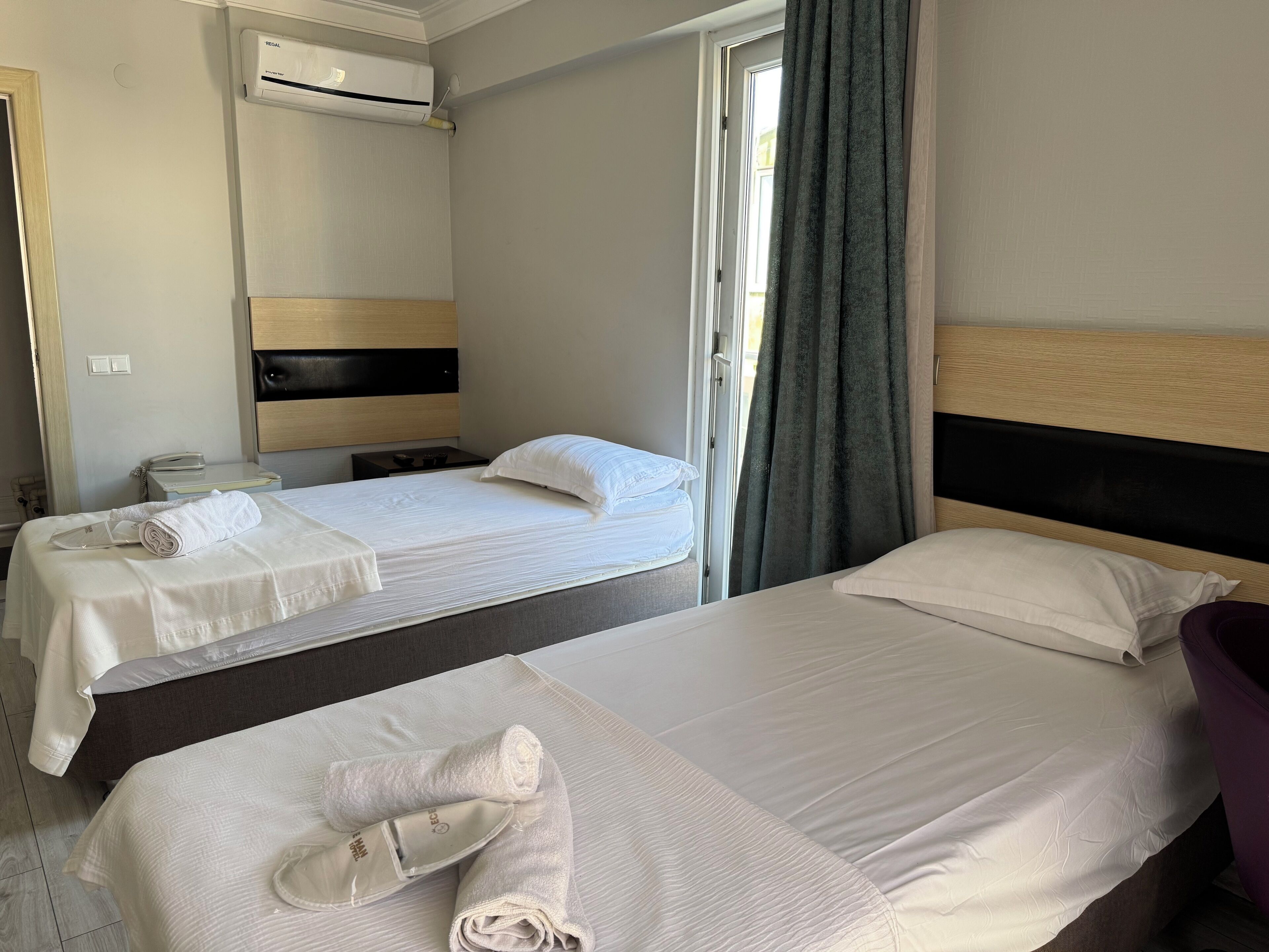 A hotel room with two beds, a bathroom, and a window with curtains.