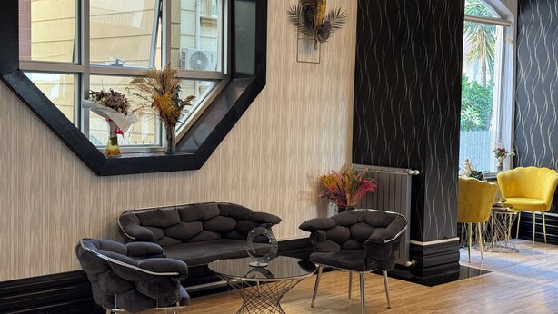 Un interior moderno con un ventanal octogonal grande, un conjunto de sofá negro, una mesa redonda de vidrio y un sillón amarillo.