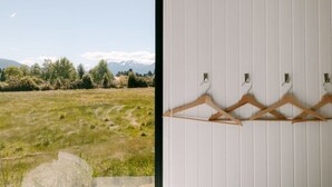 Ein Zimmer mit Blick auf ein grasbewachsenes Feld und Berge. An einer weißen Wand hängen Holzkleiderbügel.