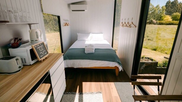 Ein gemütlicher Raum mit Bett, einer kleinen Küchenzeile und einem großen Fenster mit Blick ins Freie.