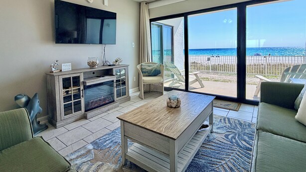A living room with a TV, fireplace, and a view of the beach.
