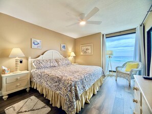 A bedroom with a bed, bedside lamps, a nightstand, a dresser, a chair, and a view of the ocean. - Gulfgate 201 - Stay BEACH Front on the Gulf! (Panama City Beach)