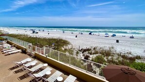 A beach with white sand, ocean waves, and a clear sky. There are lounge chairs and umbrellas on the beach.