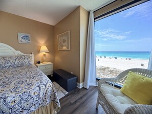 Une chambre à coucher avec un lit, une table de chevet, une lampe et une vue sur la plage.