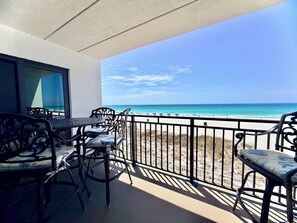 A balcony with a view of the beach, a table, and chairs.