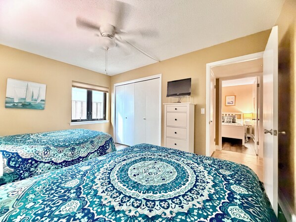A bedroom with two beds, a ceiling fan, a wardrobe, a television, and a window with blinds.