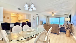 Un salon moderne avec une table à manger en verre, des chaises en osier, un canapé et une vue sur la mer.