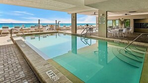 A pool area with lounge chairs and a view of the ocean.