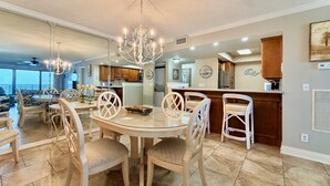 A spacious dining area with a round table and chairs, a chandelier, and a view of the outdoors.
