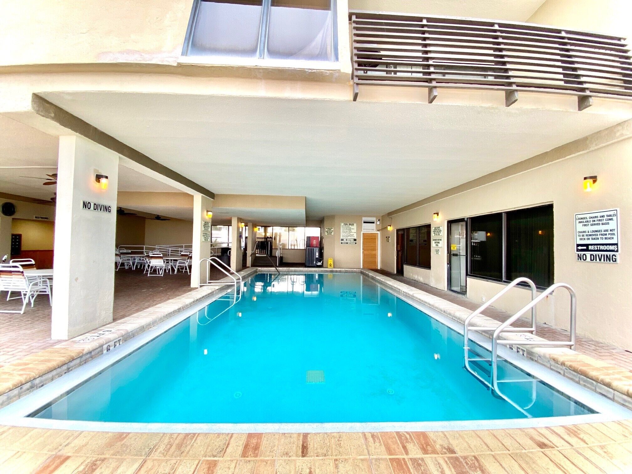 An indoor swimming pool with a 'No Diving' sign, lounge chairs, and tables.