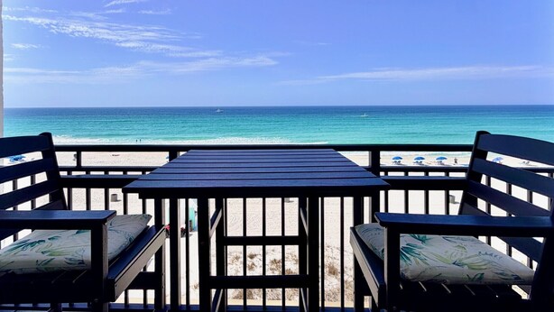 Blick auf einen Strand von einer Terrasse mit Tisch und Stühlen, mit Blick auf das Meer.