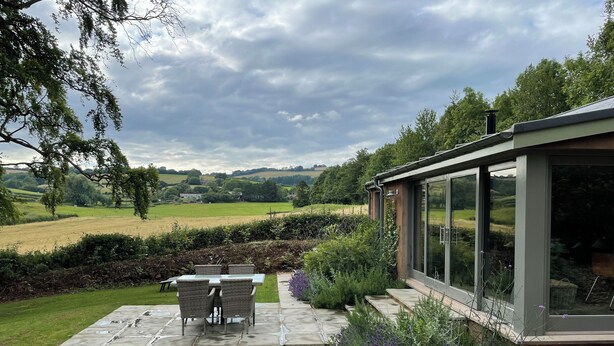 A patio with a table and chairs, surrounded by a garden with gravel and plants, and a view of the countryside. - Court Lodge (Taunton)