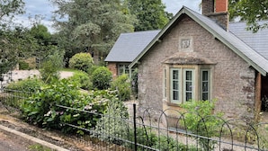 A stone house with a sloped roof, a small porch, and a window with green shutters. - Court Lodge (Taunton)