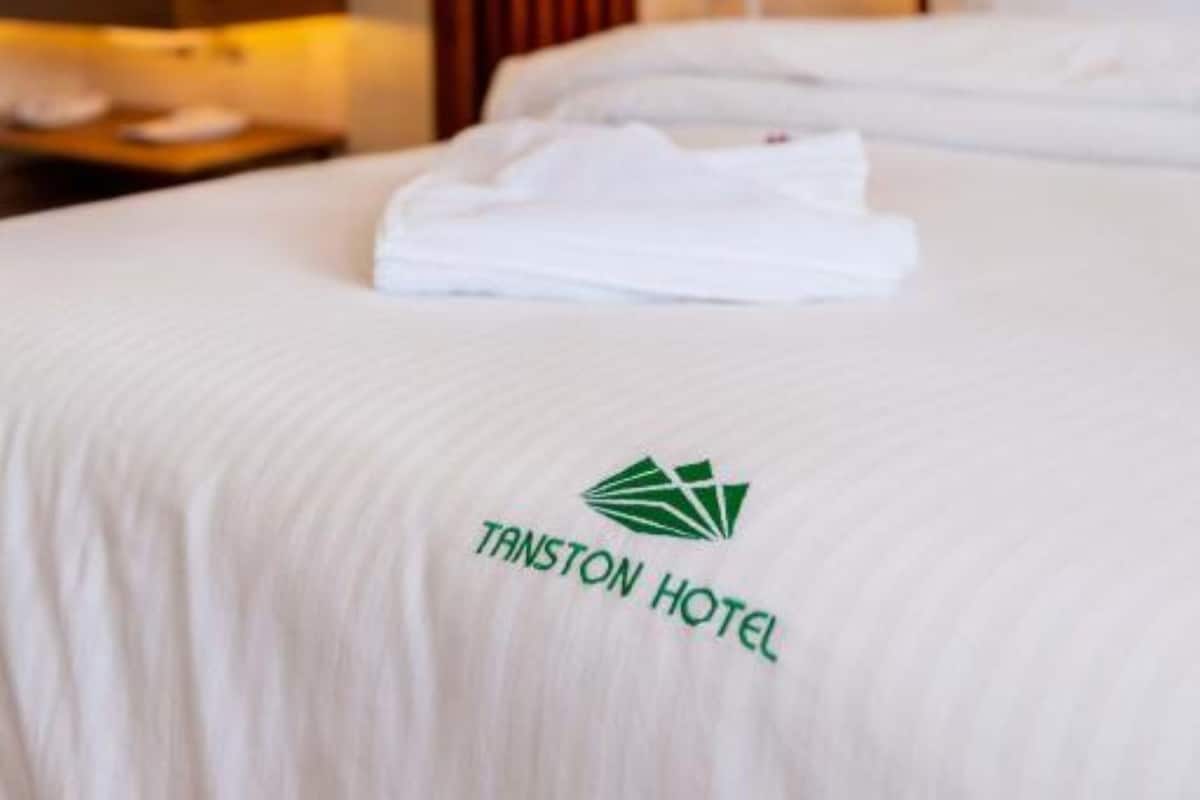 A hotel room with a neatly made bed, a bedside table with a lamp, a mirror, and a bathroom vanity with a sink.