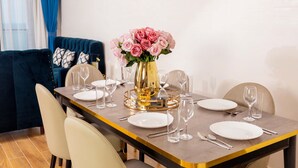 Un coin repas avec une table dressée pour quatre personnes, un vase rempli de fleurs roses et, au fond, un canapé bleu.