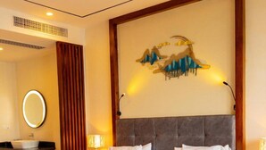 Une chambre d’hôtel avec un grand lit, un miroir rond, une commode de salle de bain et une œuvre d’art accrochée au mur.