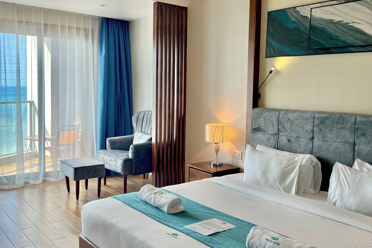 A hotel room with a large bed, a desk, a chair, a nightstand, and a view of the outdoors.