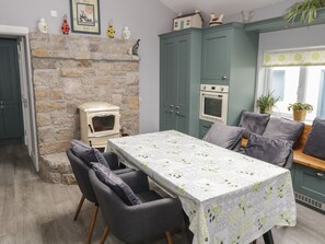 A cozy kitchen with a stone fireplace, a dining table with chairs, and a built-in oven. - Tí Coilín Mhac (Maumeen)